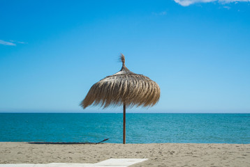 Wall Mural - A straw umbrella at the beach with perfect sand and blue sea at Torremolinos (Malaga province, Andalusia, Spain).