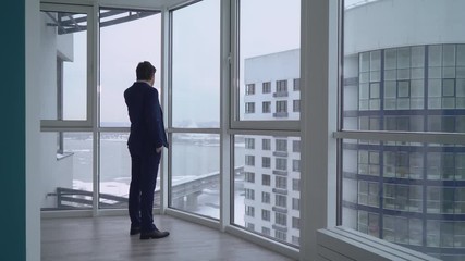 Poster - Adult man talking using mobile phone. caucasian businessman walking by big panoramic windows with urban view on the city.