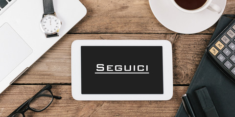 Wall Mural - Seguici, Italian text for Follow Us on screen of tablet computer at office desk