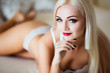 Seductive portrait. Beautiful young blonde woman with red lips posing on bed in luxury interior wearing seductive white lingerie.