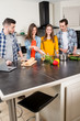© W PRODUCTION - group of friends, four people man and woman at home cooking, drinking wine and preparing food meal together in the kitchen