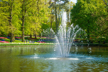 Pond With A Fountain In The Keukenhof Park In Netherlands. In The Background To Blur The Tourists Walk In The Park Keukenhof, Holland, Netherlands.