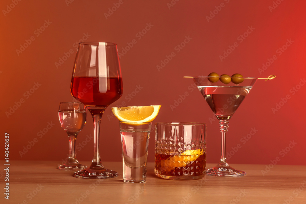 Table with glasses of wine and spirits on color background
