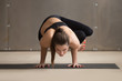 © fizkes - Young attractive yogi woman practicing yoga, standing in Parsva Bakasana exercise, Side Crane pose, working out, wearing black sportswear, cool urban style, full length, grey studio background