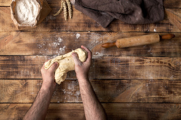Poster - Male hands knead the dough on a wooden table