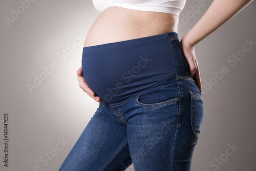 Zdjęcie XXL Kobieta w ciąży w niebieskich dżinsach dla kobieta w ciąży na szarym tle