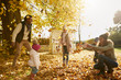 Family Playing With Autumn Leaves In Garden Together