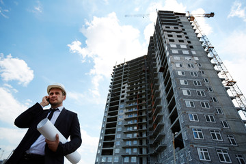 Sticker - Elegant investor in helmet talking on mobile phone by unfinished building