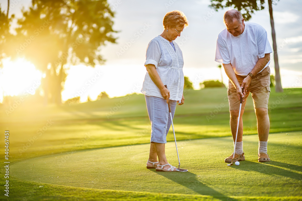 active senior lifestyle, elderly couple playing golf together at sunset - obrazy, fototapety, plakaty 