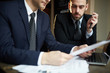 © pressmaster - Closeup portrait of two successful business partners wearing black formal suits working during meeting: reading documents and discussing deal