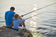 © pressmaster - Back view portrait of adult man and teenage boy sitting together fishing with rods in calm glittering waters of blue lake on sunny summer day
