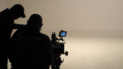 Behind the scenes of silhouette working people or video production film crew are making movie or shooting commercial with high quality professional equipment in studio.