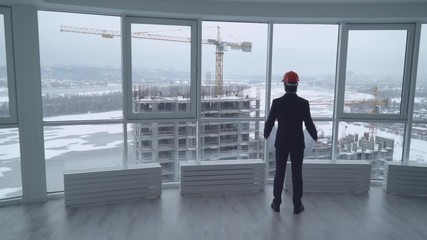 engineer architect looking on the plan. rear back view man in the office looking through the windows on the construction the high rise house wearing in suit and hard hat. Male in developer company