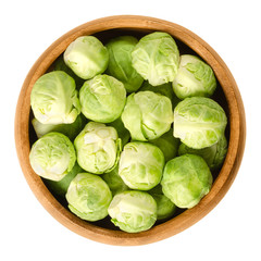 Wall Mural - Brussels sprouts in wooden bowl. The leafy green vegetables look like miniature cabbages. Raw edible buds, member of Gemmifera group. Isolated macro food photo close up from above on white background.