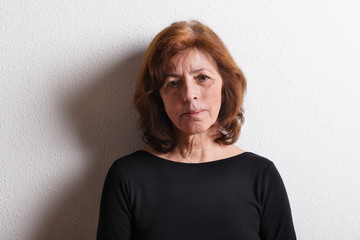 Senior woman in black t-shirt, studio shot against white wall.