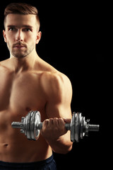 Poster - Sporty man doing exercises with dumbbell on black background