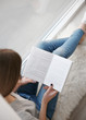 © Africa Studio - Young woman reading book on windowsill at home