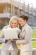 © MDBPIXS - Happy young businesswomen using laptop together against building