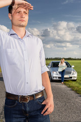 Wall Mural - Young man shielding eyes with woman and car in background at countryside