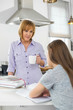 © MDBPIXS - Mother holding coffee cup while looking at girl studying in kitchen