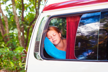 A beautiful red-haired girl is sleeping on the bus while traveling.