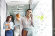 © moodboard - Young businesswoman on call with colleagues in background at office corridor