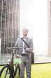 © MDBPIXS - Happy businessman standing with bicycle outside building