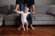 © Lisa Tichané - Smiling baby learning to walk in the living room with his mother holding his hands