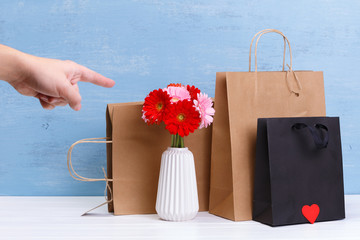 Wall Mural - Mockup of blank shopping bags. Gerbera flowers and red heart. Man points a finger. Concept for sales or discounts. Blue wooden rustic board.