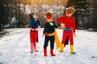 © RooM The Agency - Three children wearing superhero costumes standing side by side on a frozen lake in winter, USA