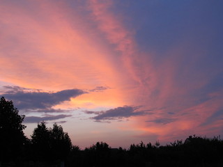 Amazing orange and blue clouds swirling swirl in the sky. Beautiful natural sunset in the country during summer heat season.