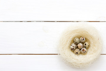 Easter quail eggs in nest on white wooden background.