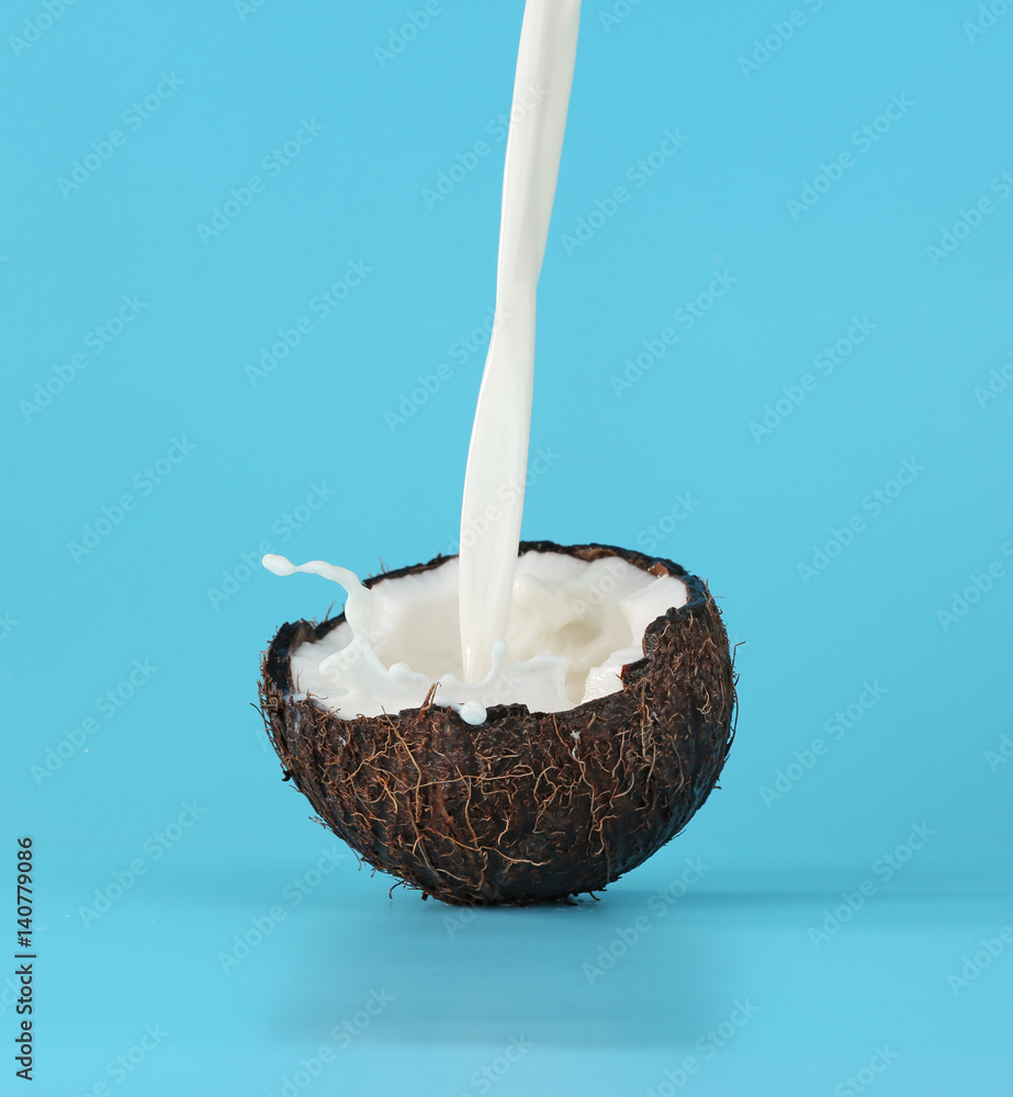 Cracked coconut with jet of milk on color background