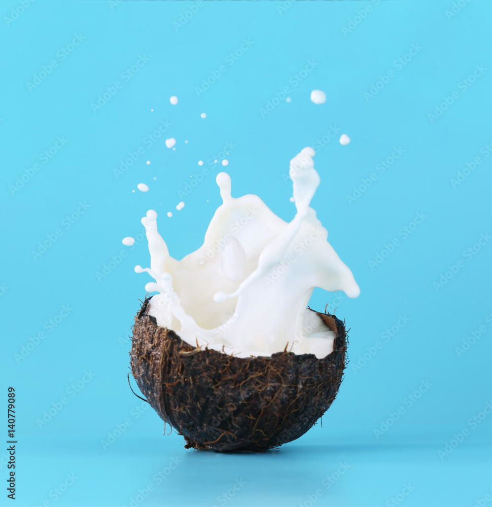 Cracked coconut with splashes of milk on color background