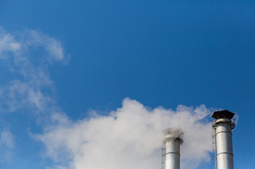 The smoke from the chimneys of a heating plant in the background of blue sky. Pollution of the environment. The exhaust emissions from the chimneys into the atmosphere