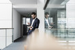 © Westend61 - Businessman standing in office building, using smart phone and digital tablet