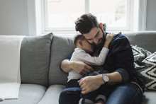 Father Embracing Son While Sitting On Sofa At Home