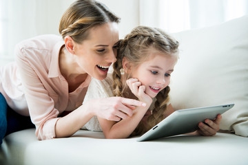 portrait of cheerful mother and daughter using tablet at home