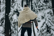 Strong Viking Warrior With Mohawk Haircut And Wolf Pelt Armor Holding Axe And Walking In Winter Woods Before Historical Battle, Scandinavian Traditional Clothing, Ancient Viking Concept
