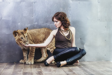 Beautiful fashionable young woman with a little alive lion cub