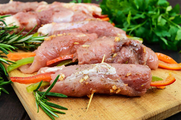 Un-cooked, pork meat rolls stuffed with vegetables (pepper, carrots) in hot garlic sauce on a cutting board. Raw, semi-finished product.