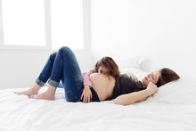 Pregnant Woman Lying On A Bed Looking At Her Daughter Cuddling Her Naked Belly