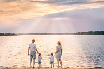 View from behind of happy family watching the sunset and sailboat on the coast of lake