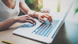 © SFIO CRACHO - Young woman working at home on modern computer while sitting at the wooden table.Female hands typing on laptop keyboard.Concept of young modern people using mobile devices at home.Blurred background.