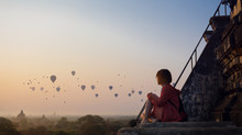 Woman Looking At Hot Air Balloons While Sitting On Stairway During Sunset