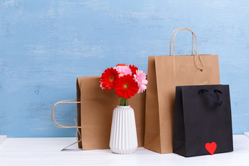 Mockup of blank shopping bags. Gerbera flowers and red heart. Brown and black craft packages. Concept for sales or discounts. Blue wooden rustic board.