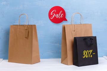 Wall Mural - Mockup of blank shopping bags. Sale speech bubble. Brown and black craft packages. Concept for sales or discounts. Recycled paper. Blue wooden rustic board.