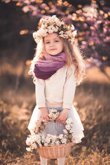 Wall Mural - Smiling kid girl 3-4 year old wearing flower wreath and holding basket with flowers outdoors. Looking at camera. Childhood.