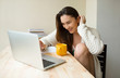 © Anton - Laughing shy girl at the table with the laptop computer drinking coffee in the cozy home clothes. Looking at the display