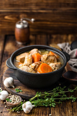 Meat stewed with carrots in sauce and spices in cast iron pot on dark wooden rustic background